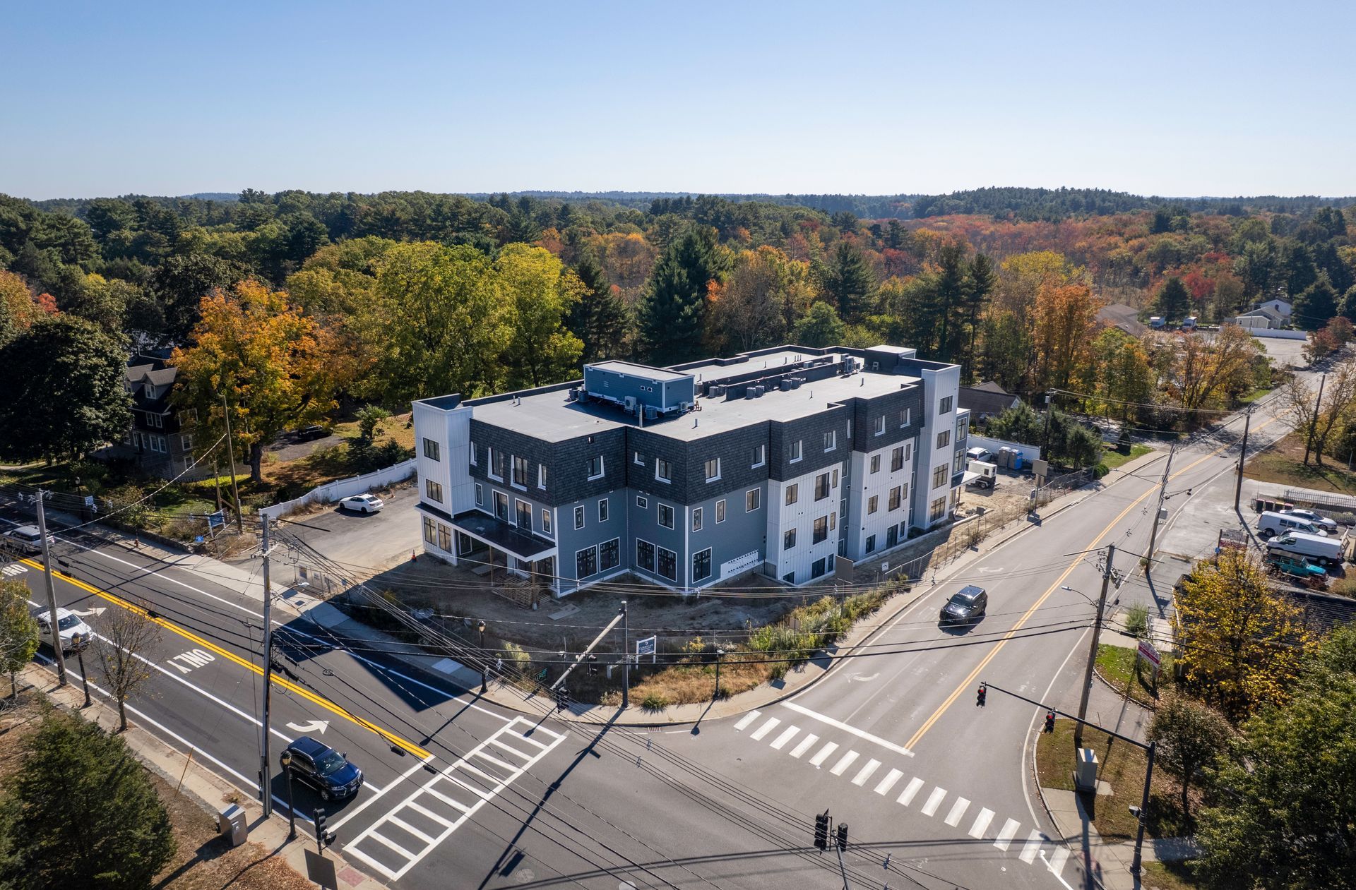 Aerial view of a four-story building at a road intersection, surrounded by trees with fall foliage.