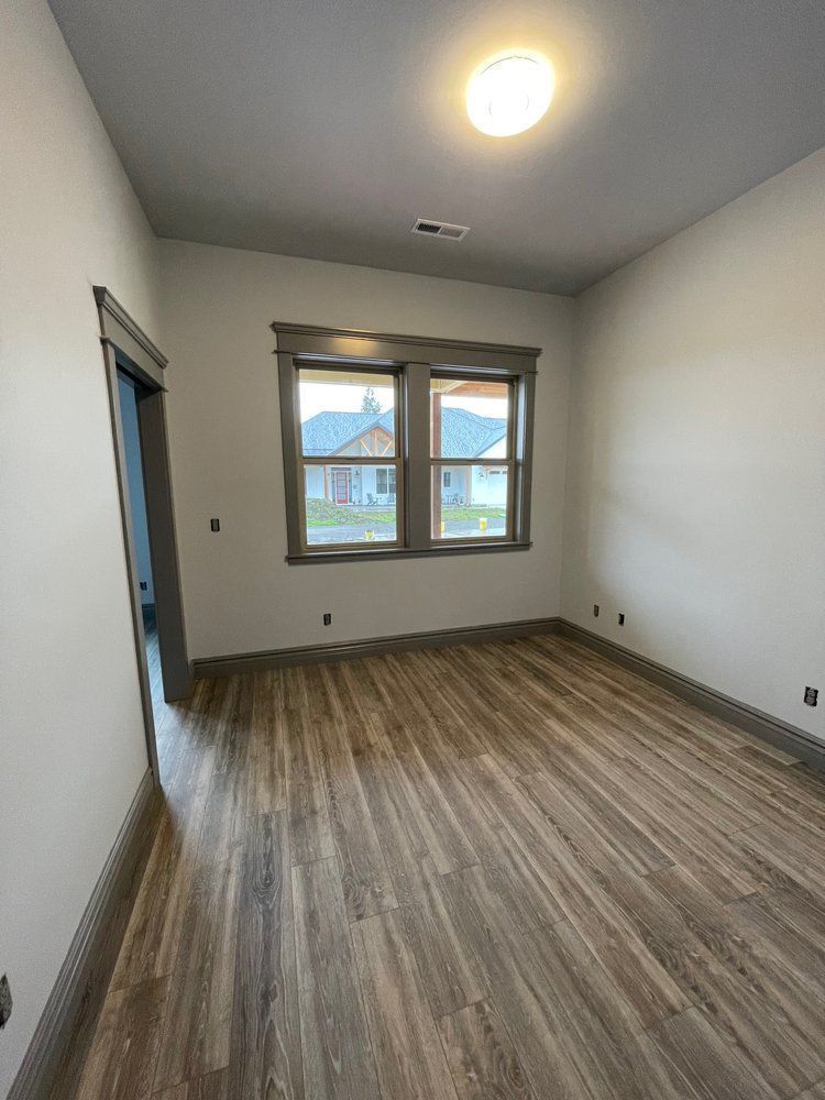 An empty room with hardwood floors and two windows.