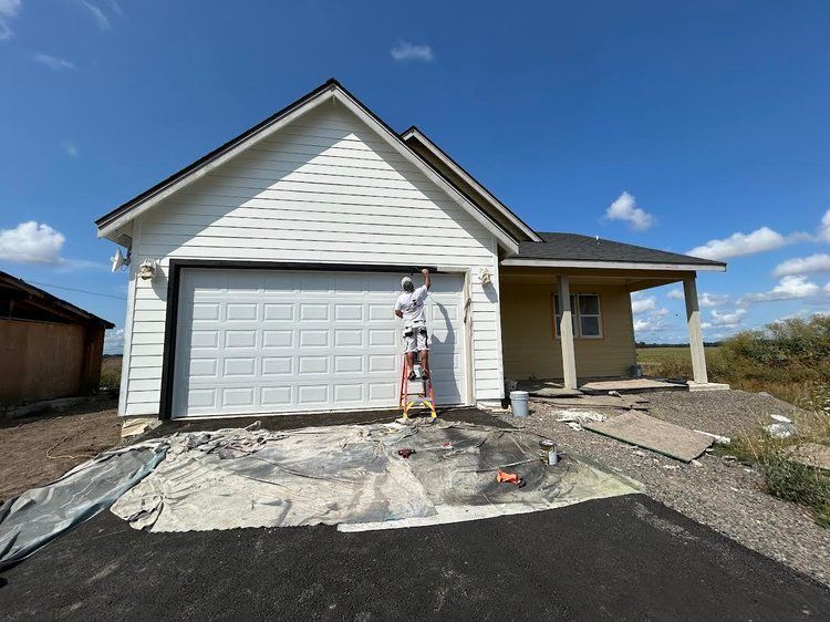 A man on a ladder is painting the side of a house.