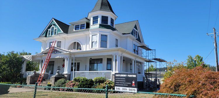 A large white house with a green roof is being painted.