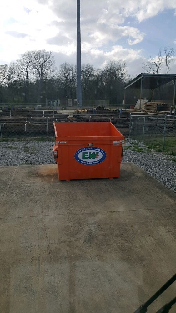A large orange dumpster is sitting on the ground in a parking lot.