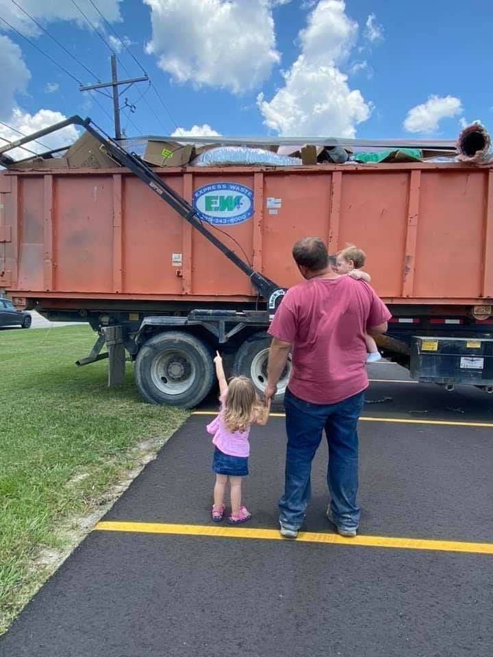 A man and two children are standing in front of a dumpster.