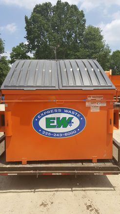 An orange dumpster with a black roof is sitting on top of a dirt field.