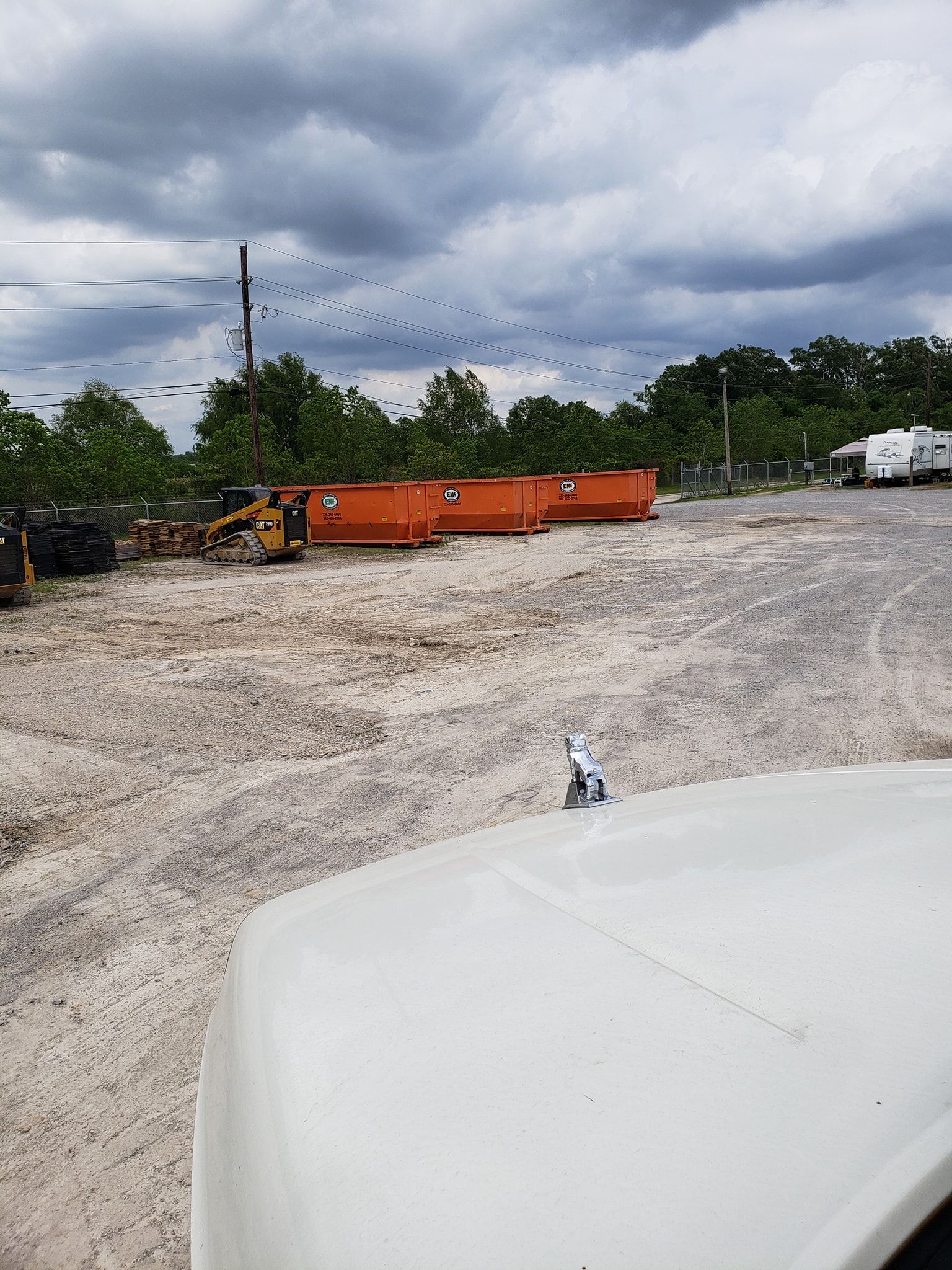 A white truck is parked in a dirt lot next to a large orange dumpster.