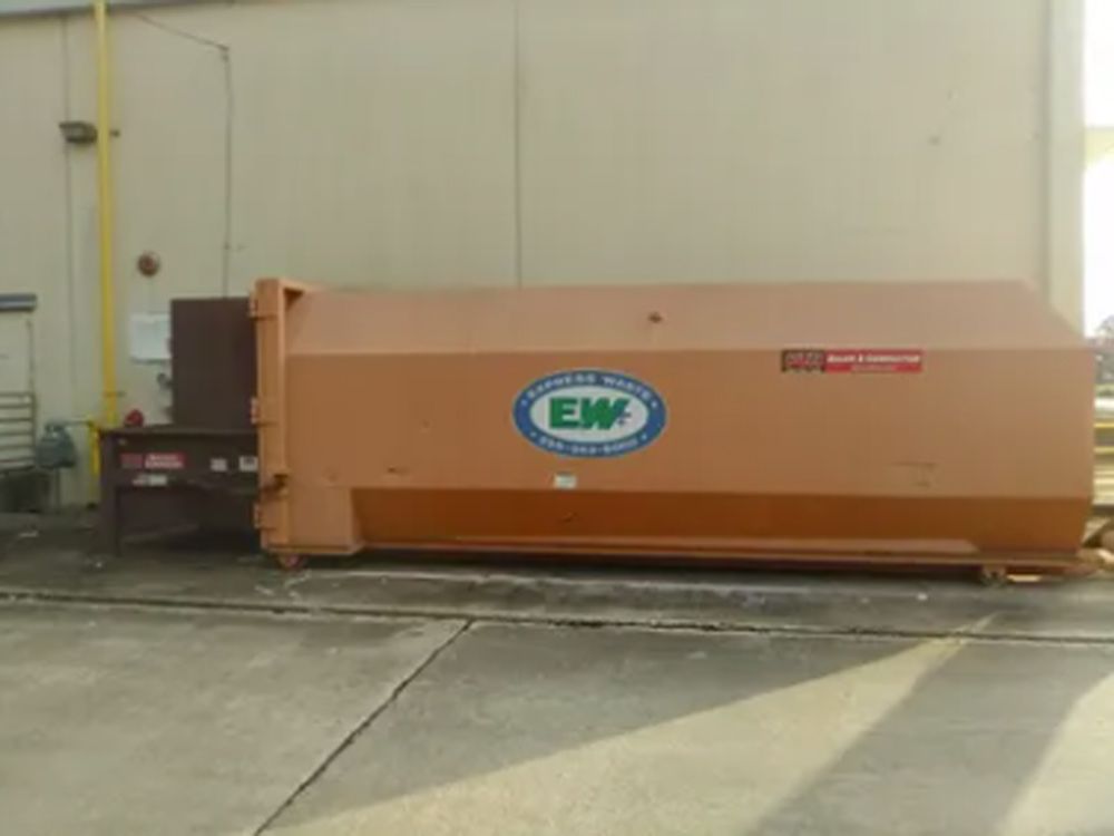 A large orange dumpster is parked in front of a building.