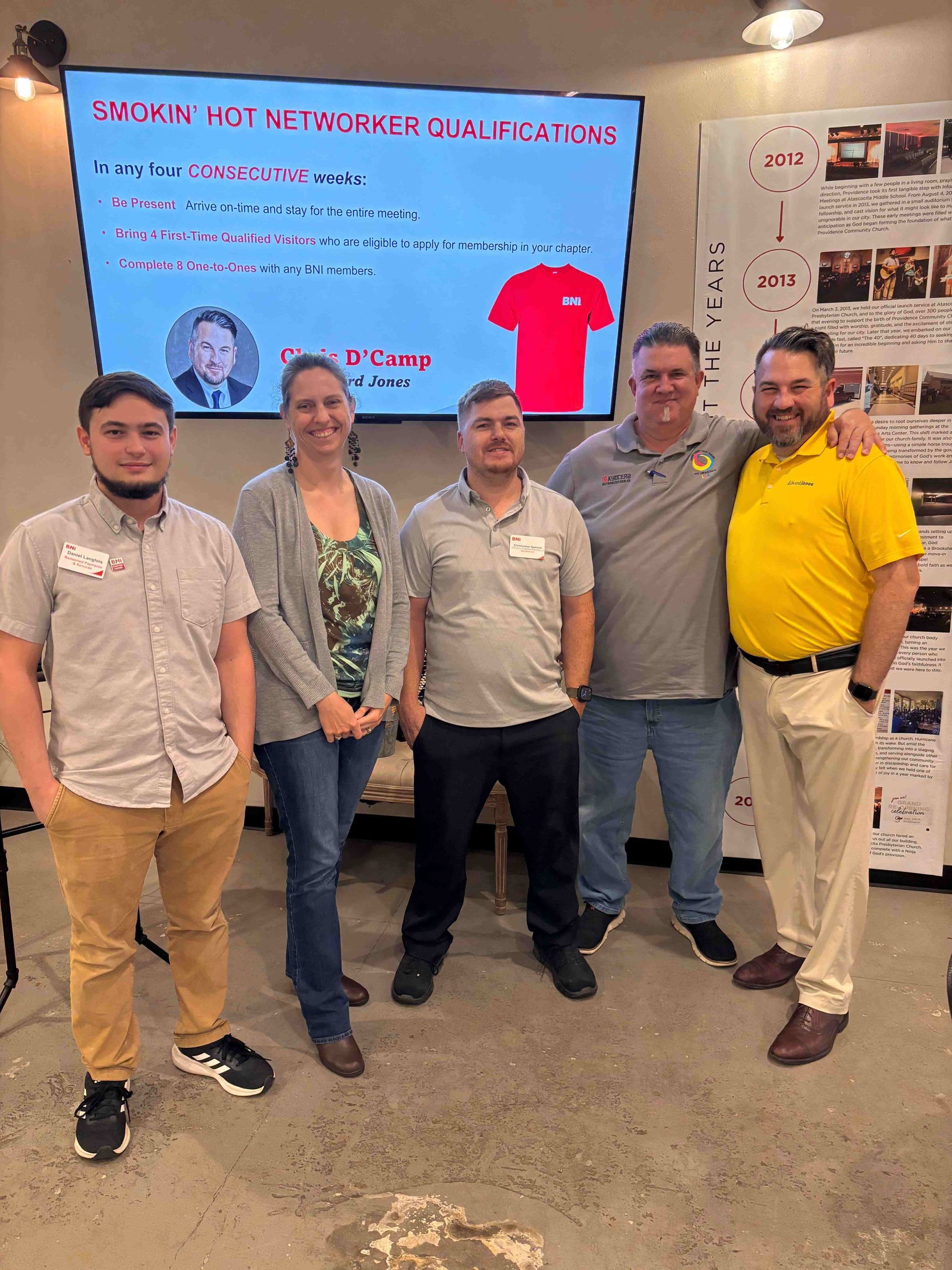 A group of people are posing for a picture in front of a large screen.