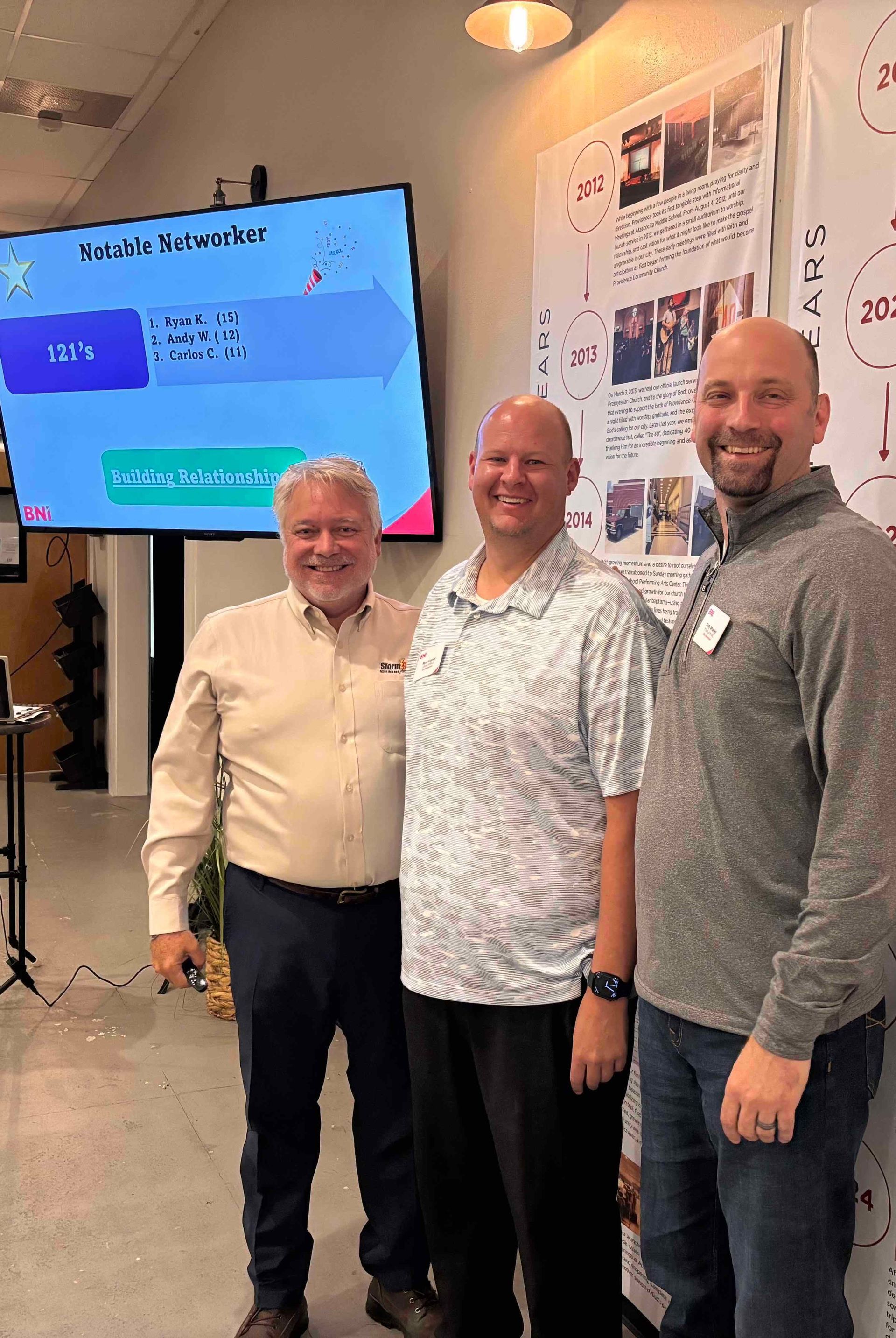 Three men are posing for a picture in front of a large screen.