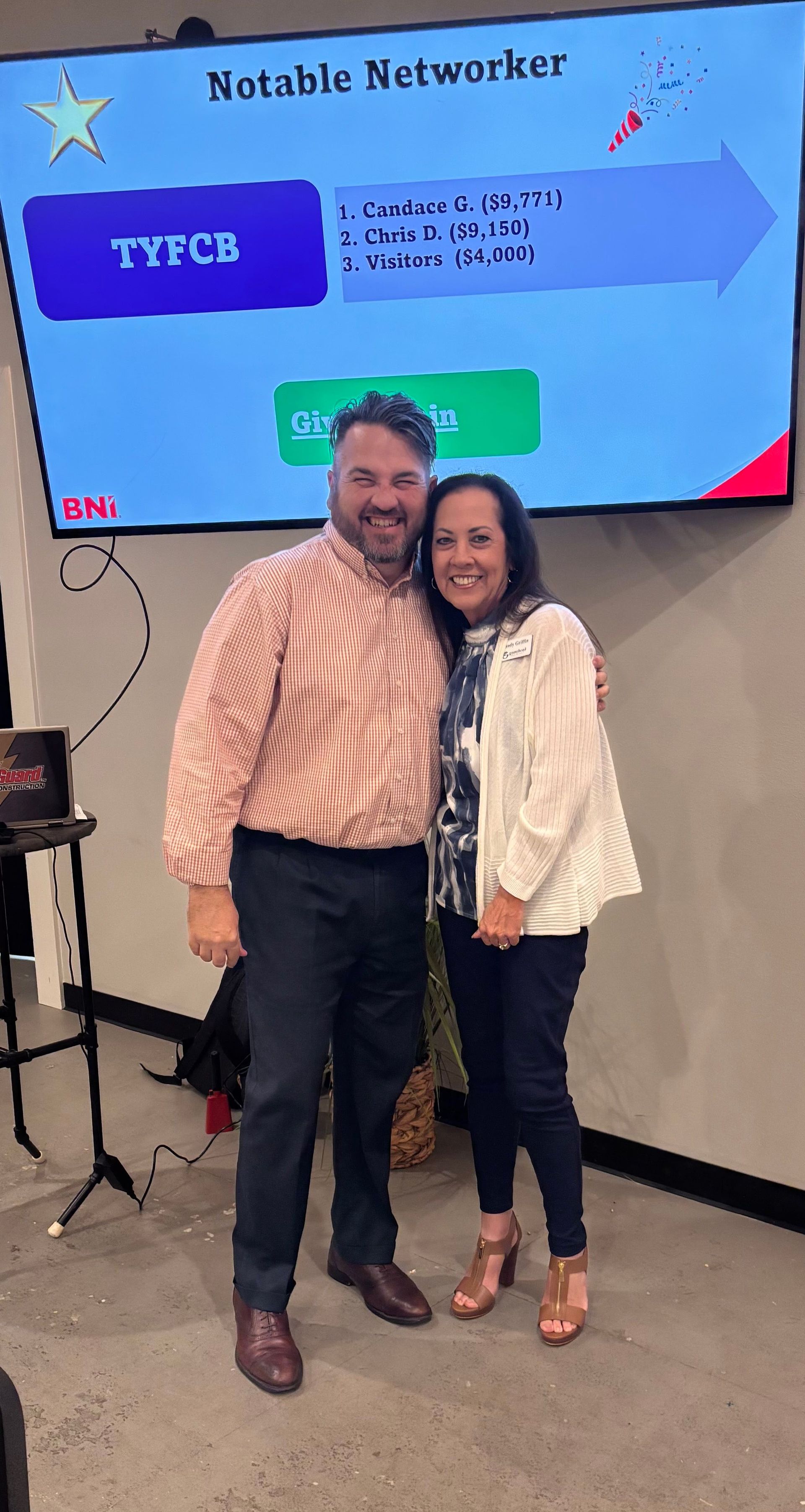 A man and a woman are posing for a picture in front of a large screen.