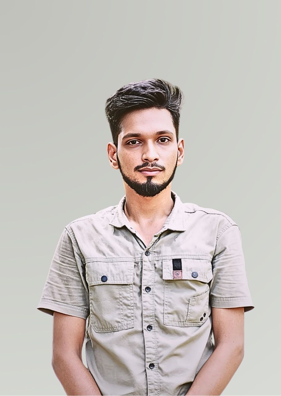 Man with dark hair and beard, wearing a light-colored shirt, standing in front of a grey background.