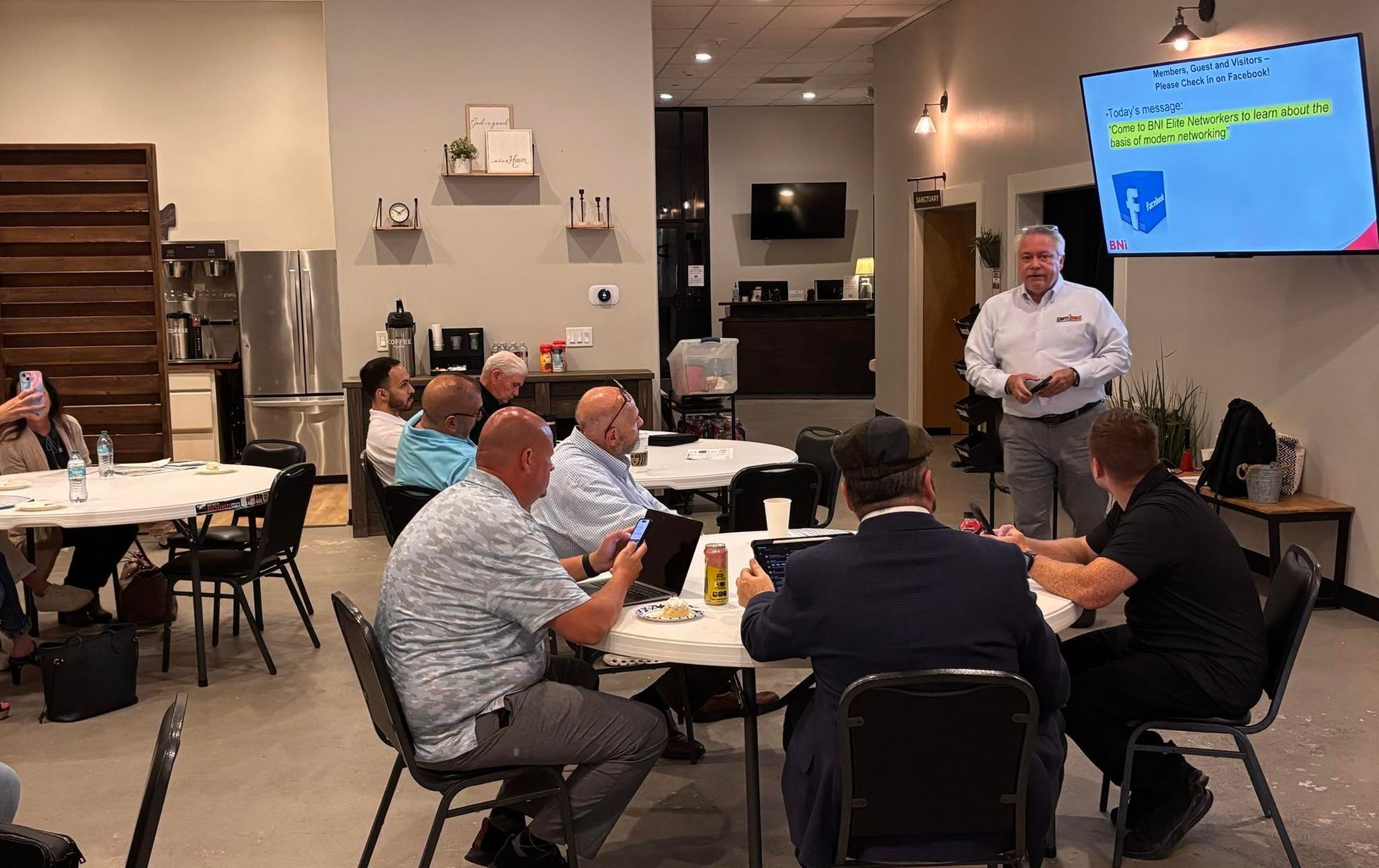 A man is giving a presentation to a group of people sitting at tables in a room.