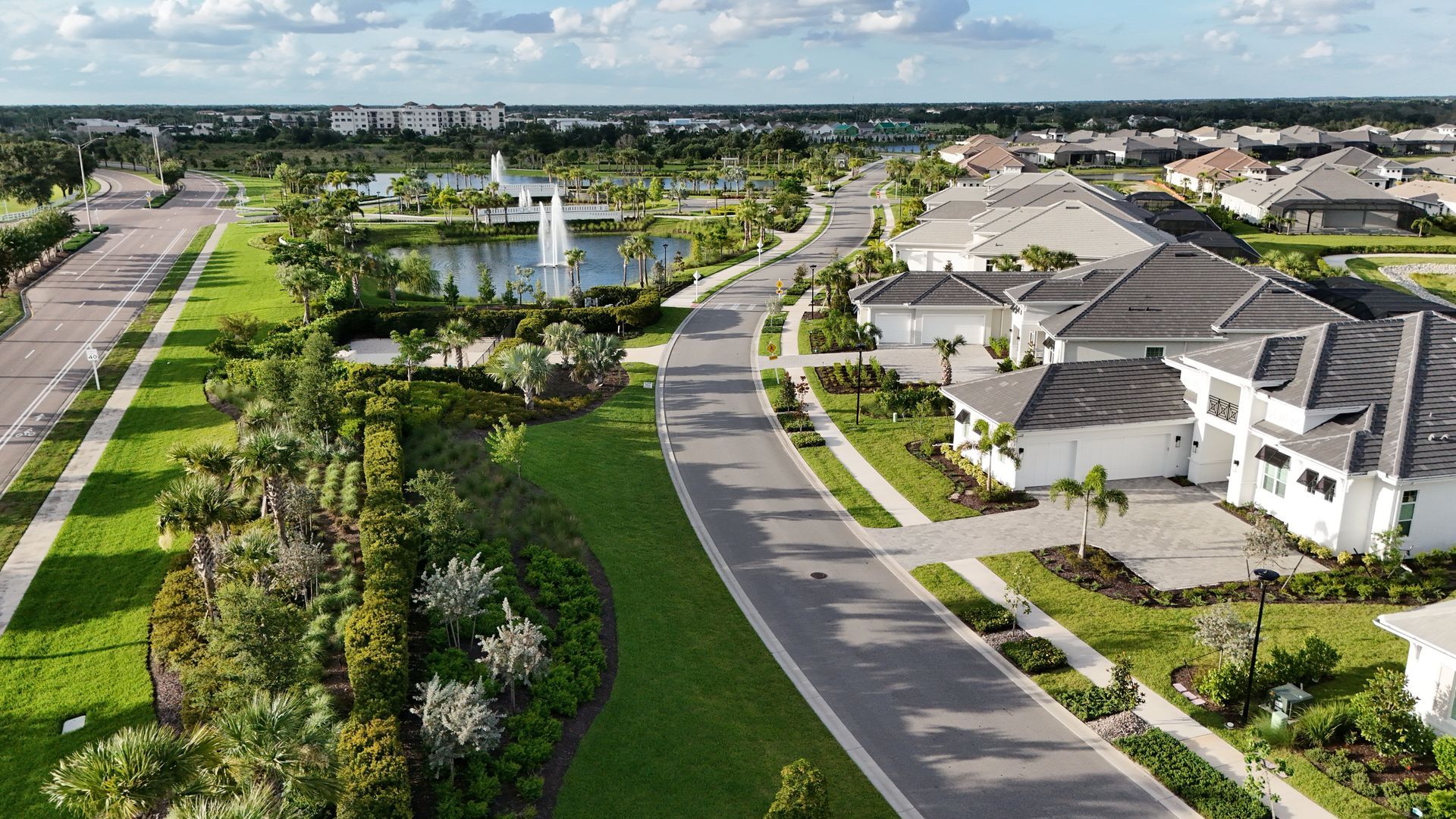 Aerial view of a suburban neighborhood with houses, roads, green spaces, and a water feature.