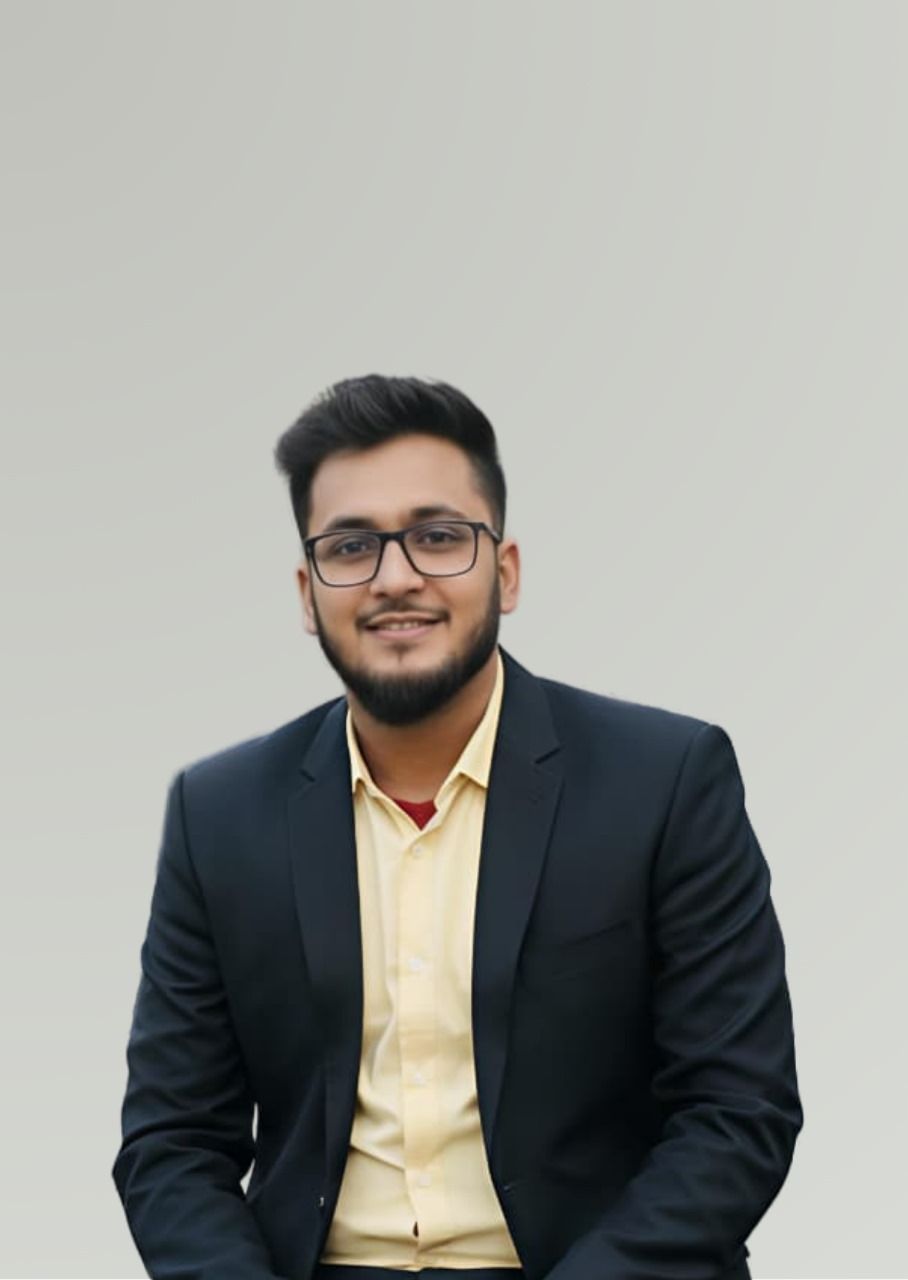 Man in black blazer and glasses smiles, posing in front of a white wall.