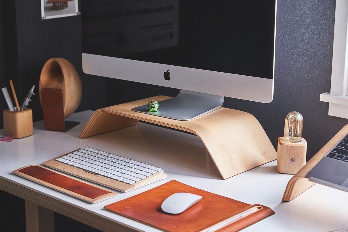 An apple computer is sitting on a wooden stand on a desk.