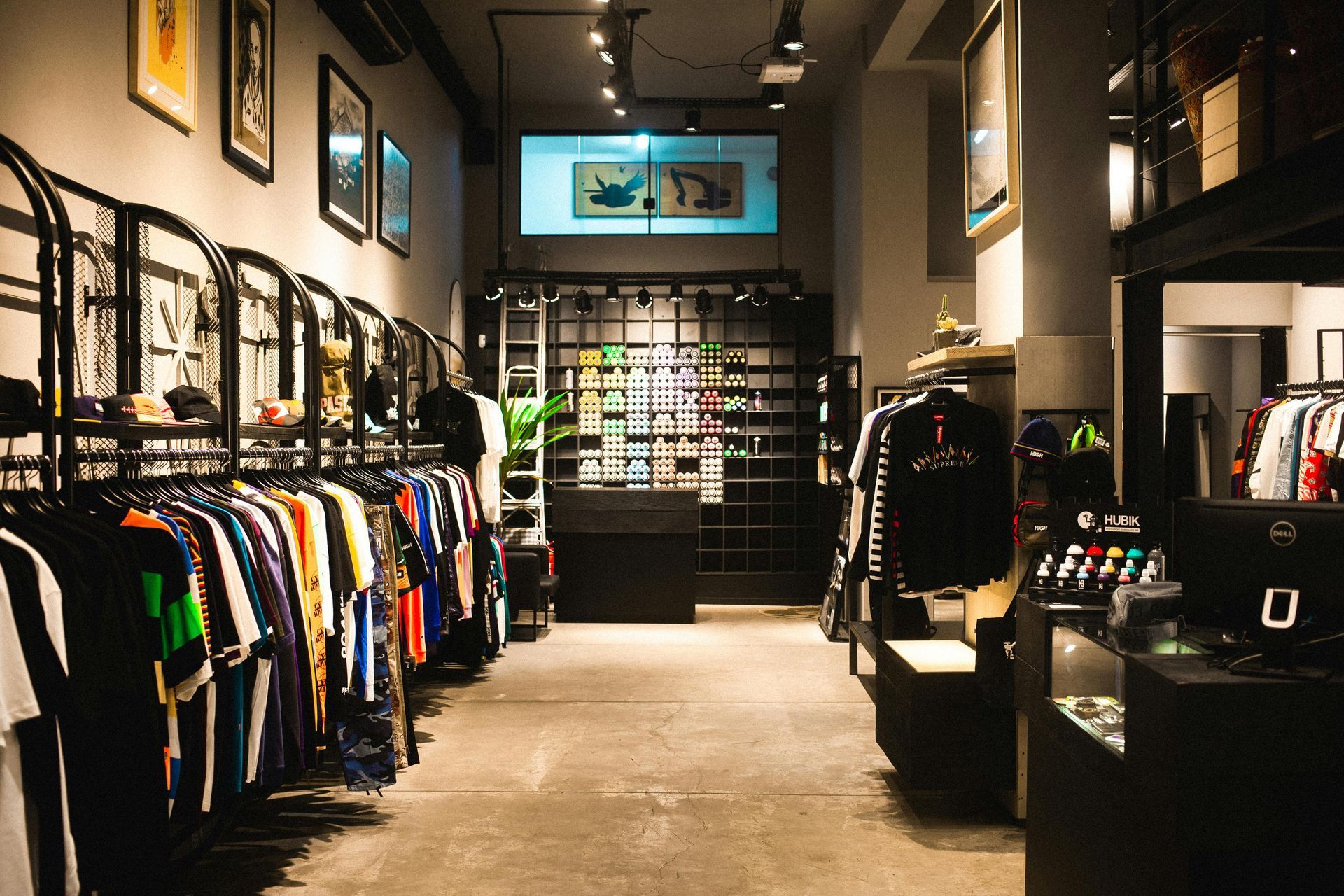 Clothing store interior with racks of apparel and displays, concrete floor, overhead lighting.