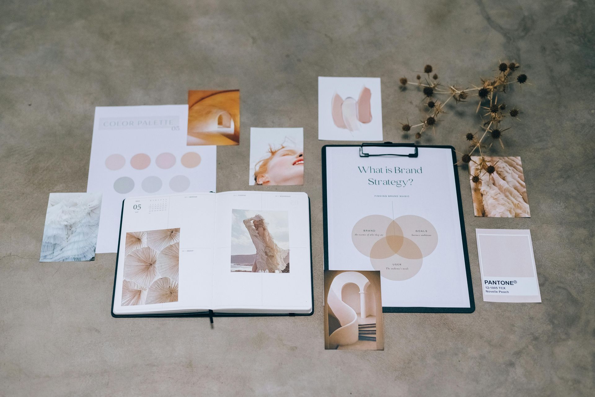 Mood board on concrete: notebook, clipboard, photos, color swatches in neutral tones.