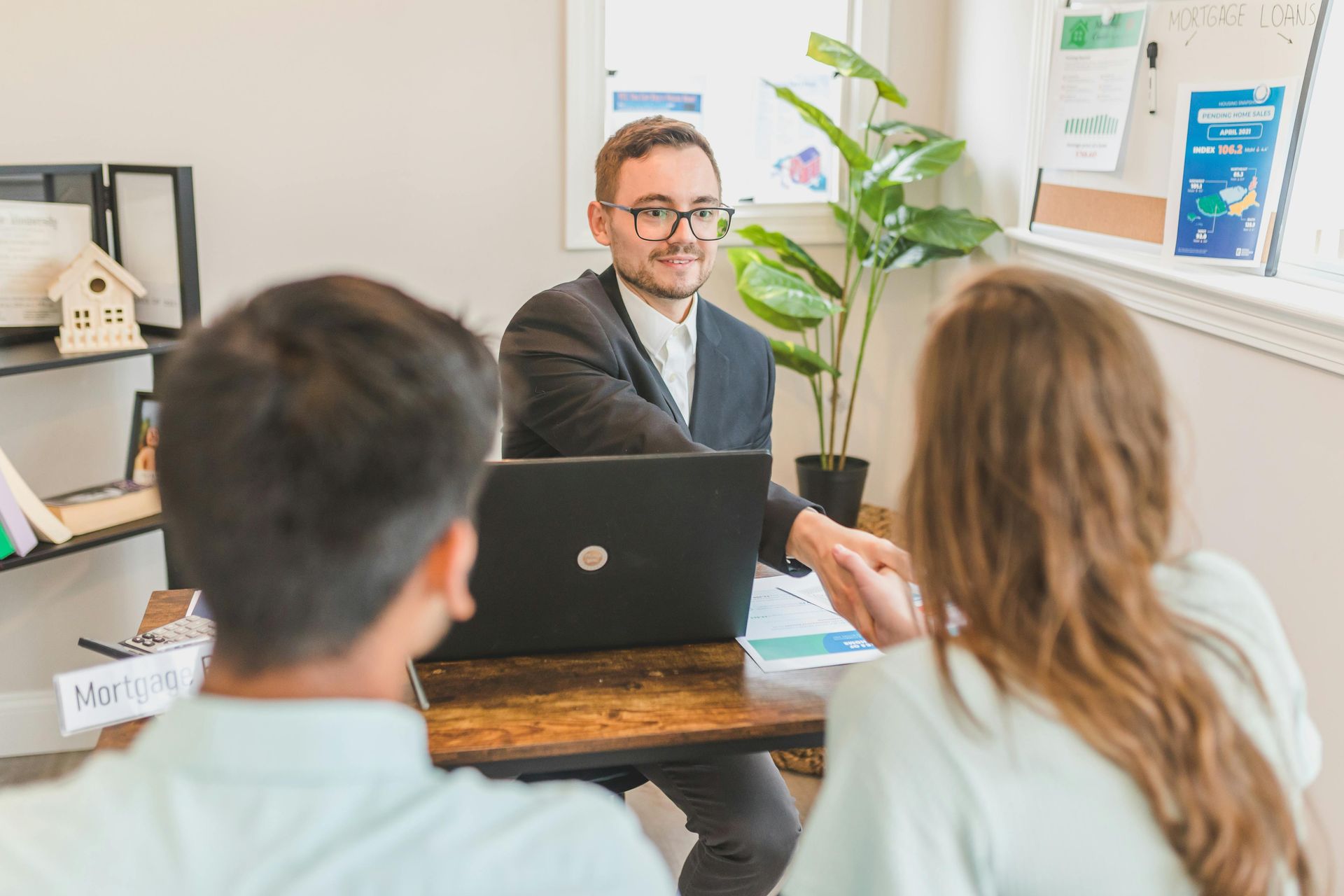 Man in suit shakes hands with a couple at a desk with a laptop and documents.