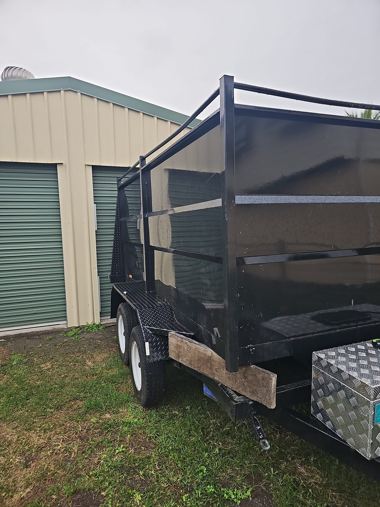 Black Dump Trailer Parked On Grass, Beige And Green Storage Units In The Background — NPX Solutions In Rockhampton City, QLD