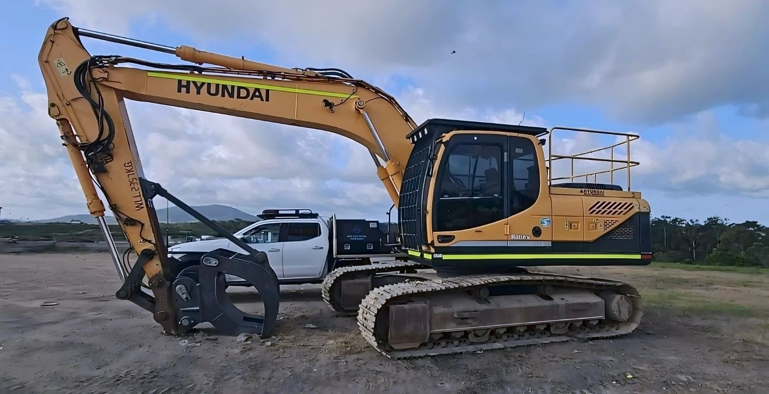 Yellow Hyundai Excavator With Grapple Attachment on a Gravel Lot, White Truck in the Background — NPX Solutions In Emerald, QLD