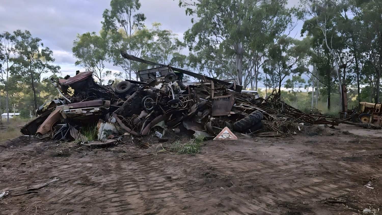 Pile of Scrap Metal and Vehicle Parts on Dirt Ground With Trees in the Background — NPX Solutions In Clairview, QLD