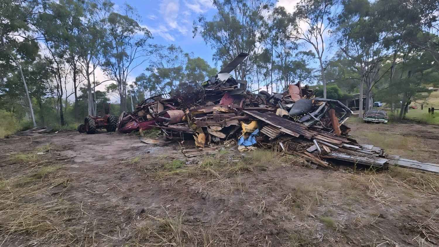 Pile of Burnt Debris on Dry Ground, Trees in Background Under a Bright Blue Sky — NPX Solutions In Gladstone, QLD