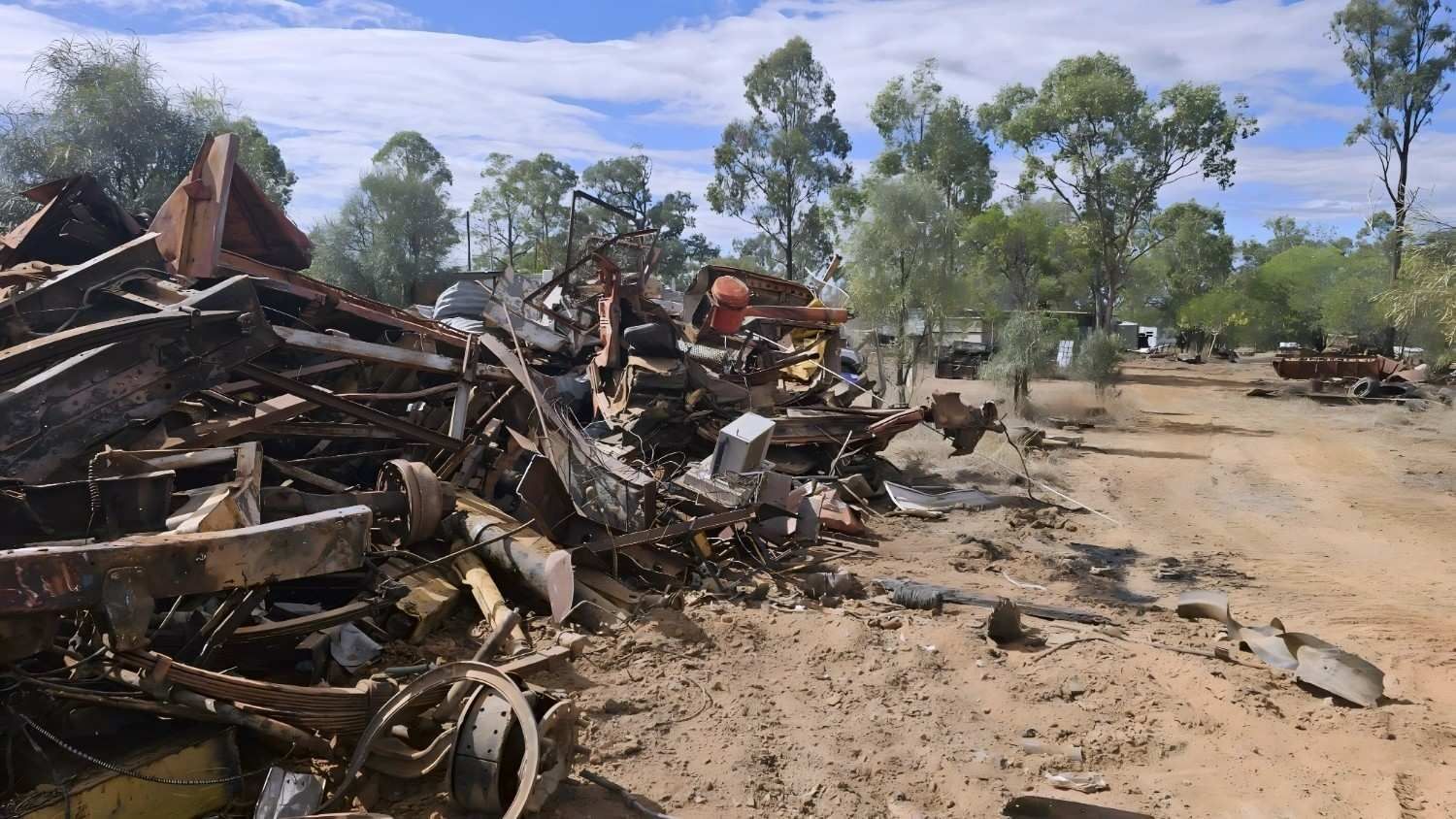 Pile of Scrap Metal and Debris Beside a Dirt Road, Trees in Background Under Blue Sky — NPX Solutions In Rockhampton City, QLD
