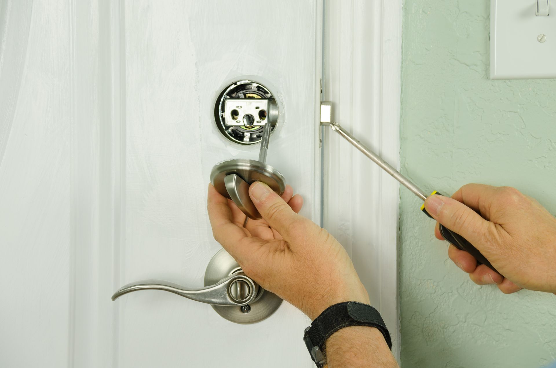 A professional locksmith repairs a deadbolt lock on a house exterior door, with internal lock parts visible.