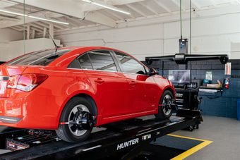 Red car on an alignment rack in a shop.