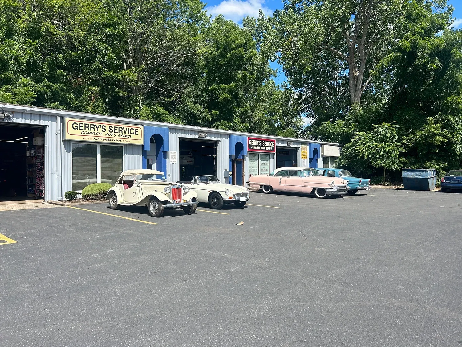 Cars parked outside an auto repair shop with multiple garage bays and a blue sky background.
