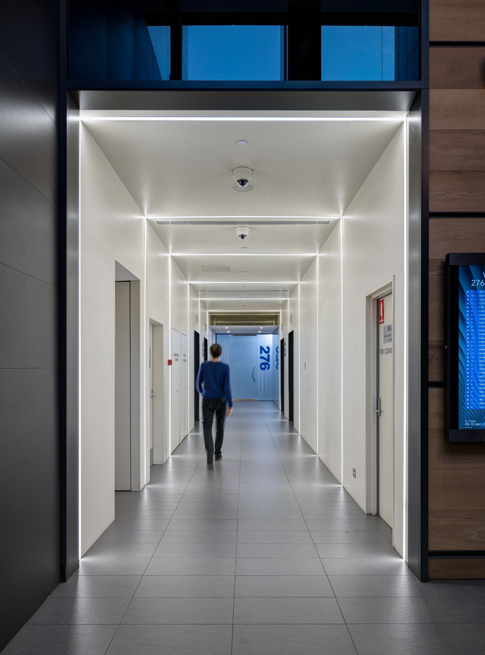 A man in a blue shirt is walking down a long hallway.