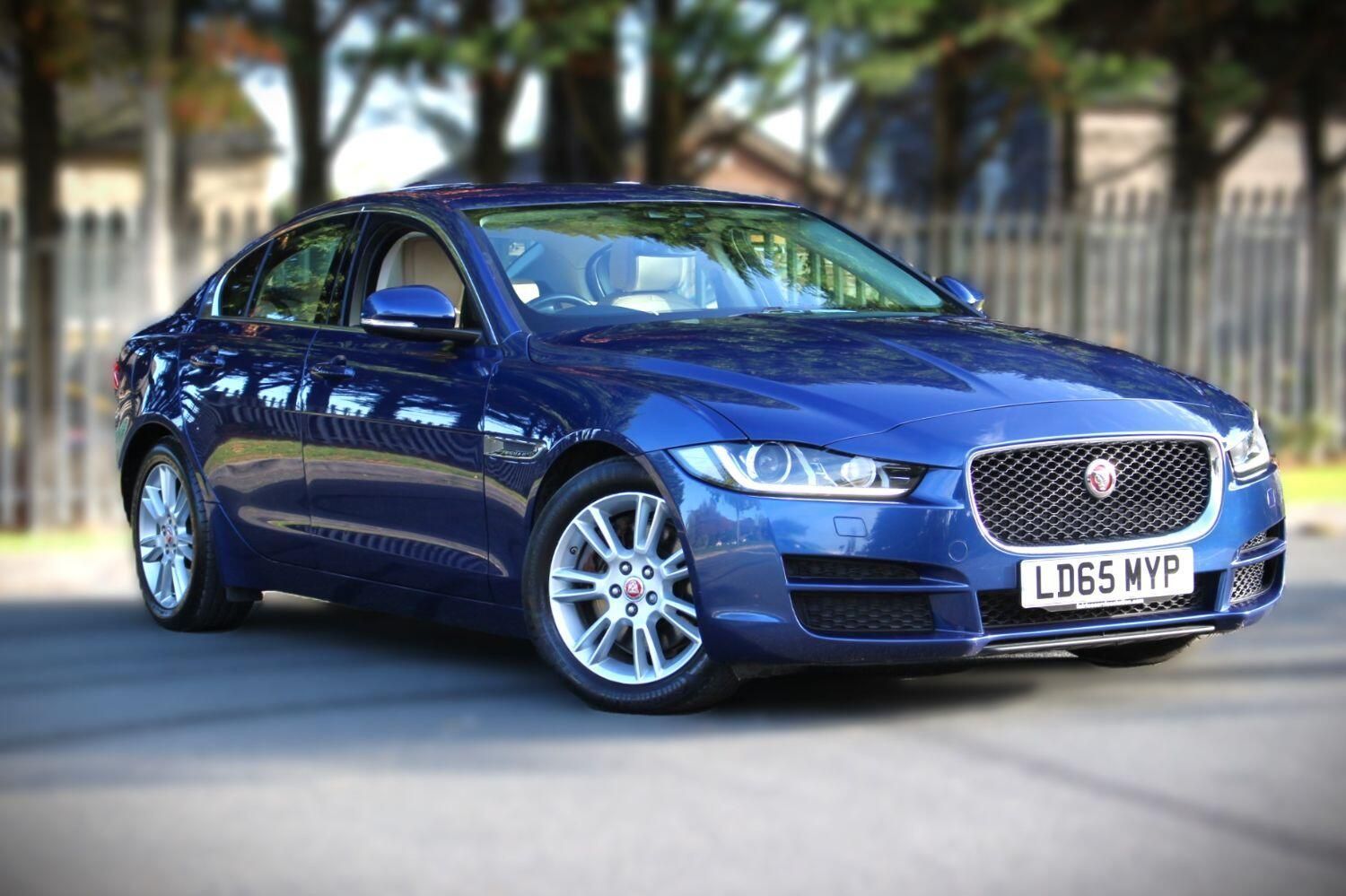 A blue jaguar car is parked in front of a fence.