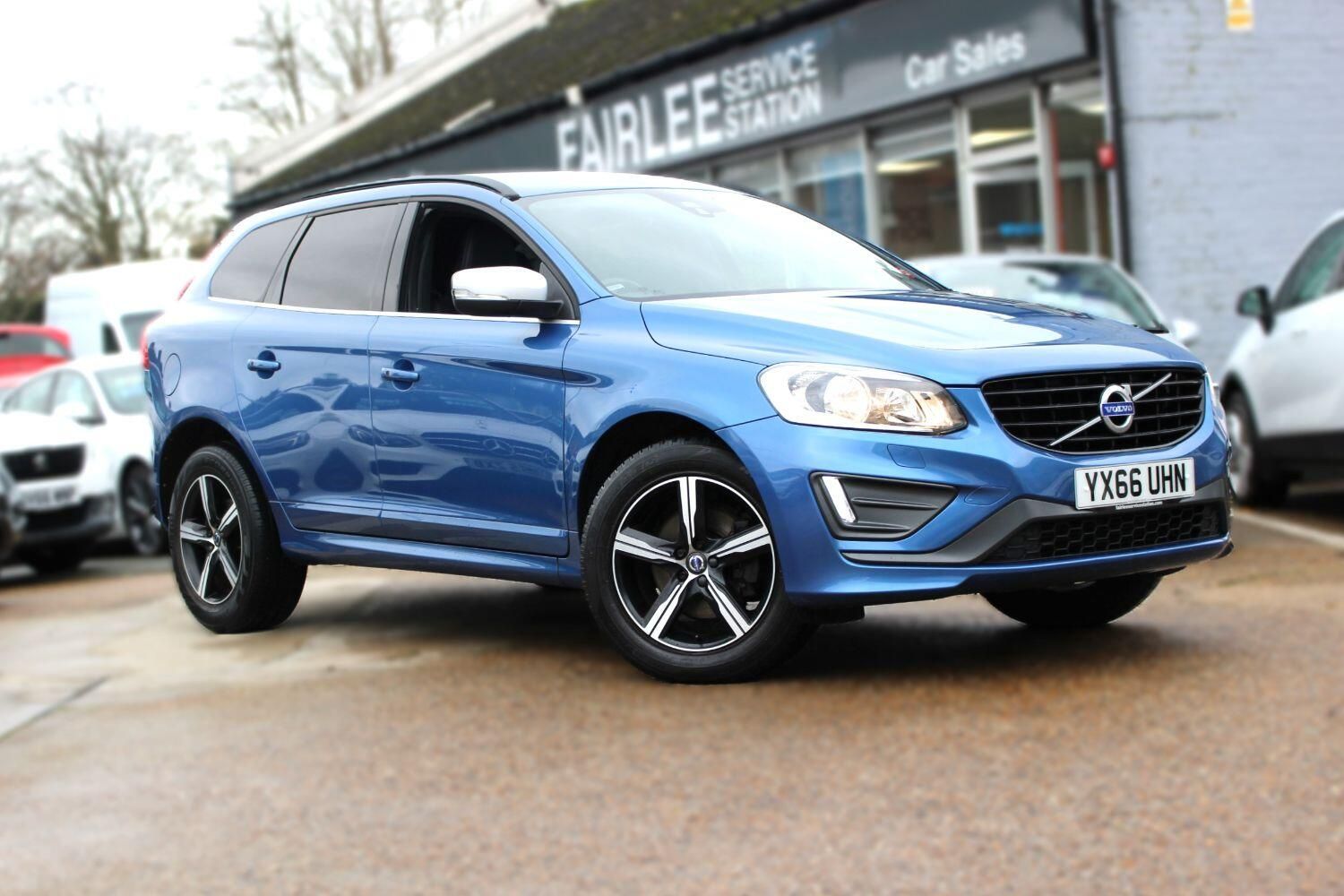A blue volvo xc60 is parked in front of a car dealership.