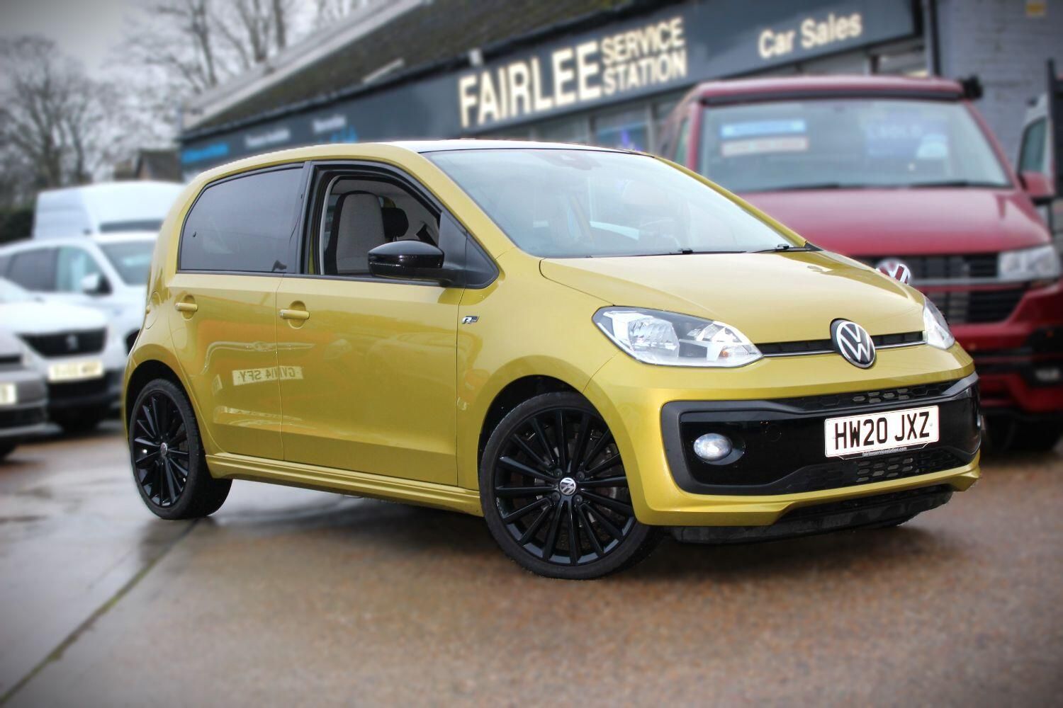 A yellow volkswagen up! is parked in front of a car dealership.