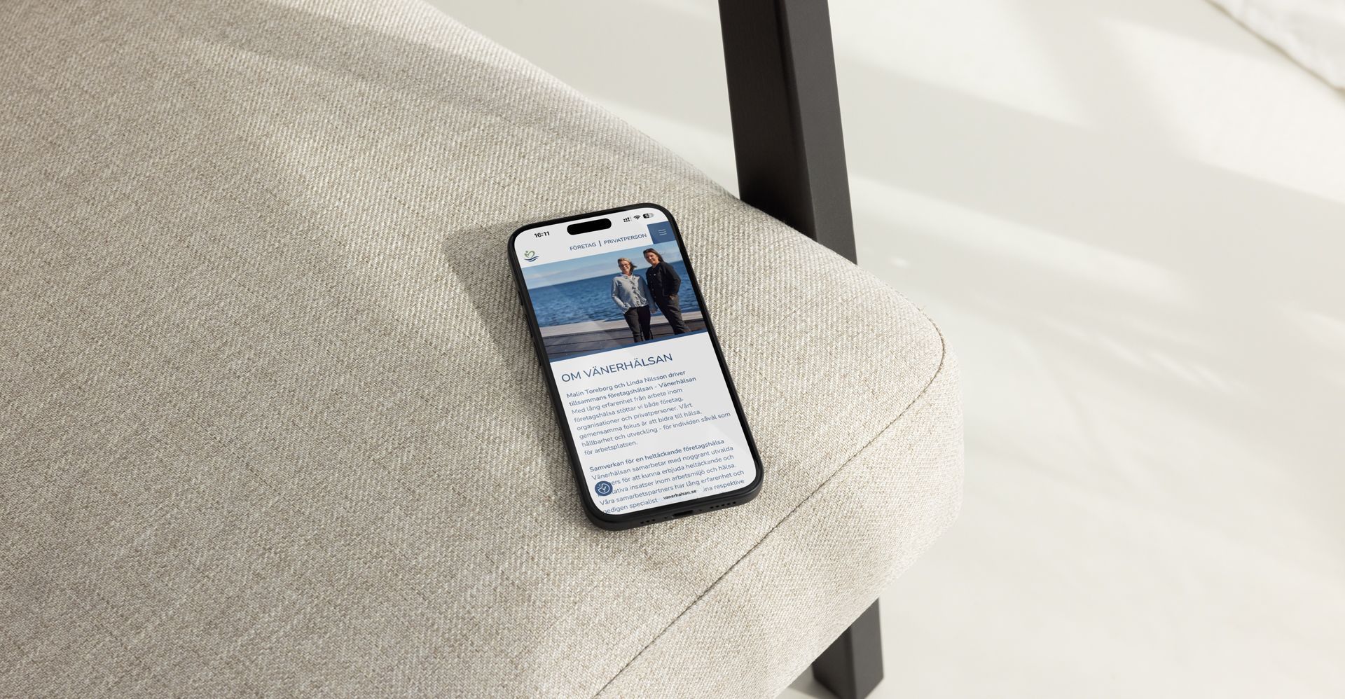 Mobil ligger p&aring; en stol med ljus textil och m&ouml;rkbrunt tr&auml;-armst&ouml;d. Visar V&auml;nerh&auml;lsans hemsida p&aring; sk&auml;rmen.