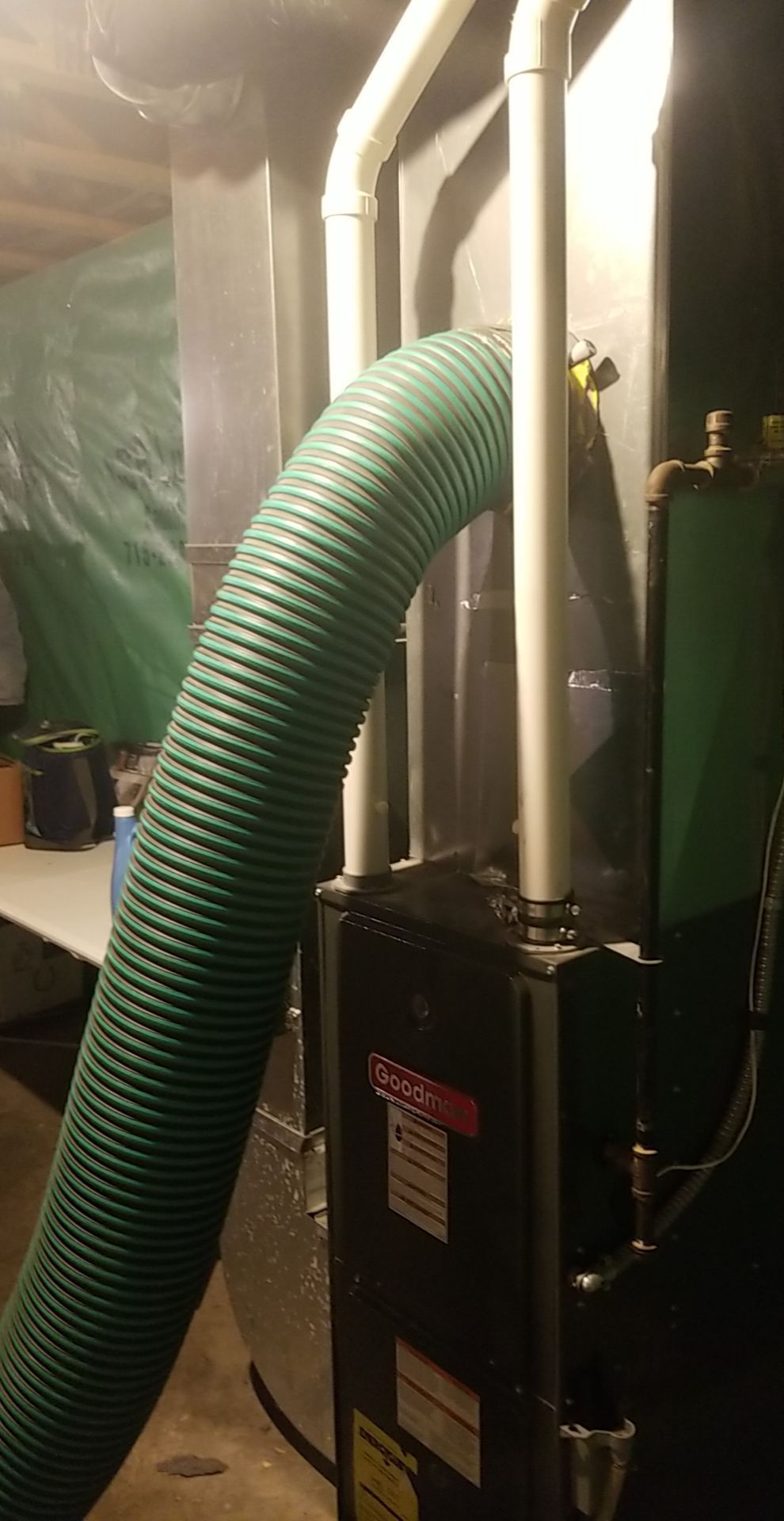 A green hose is attached to a furnace in a basement.