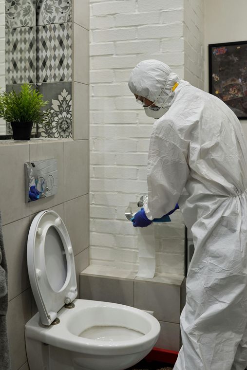 Person in hazmat suit cleaning a toilet.