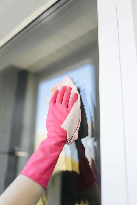 Person wearing pink glove cleaning a window with a pink cloth.