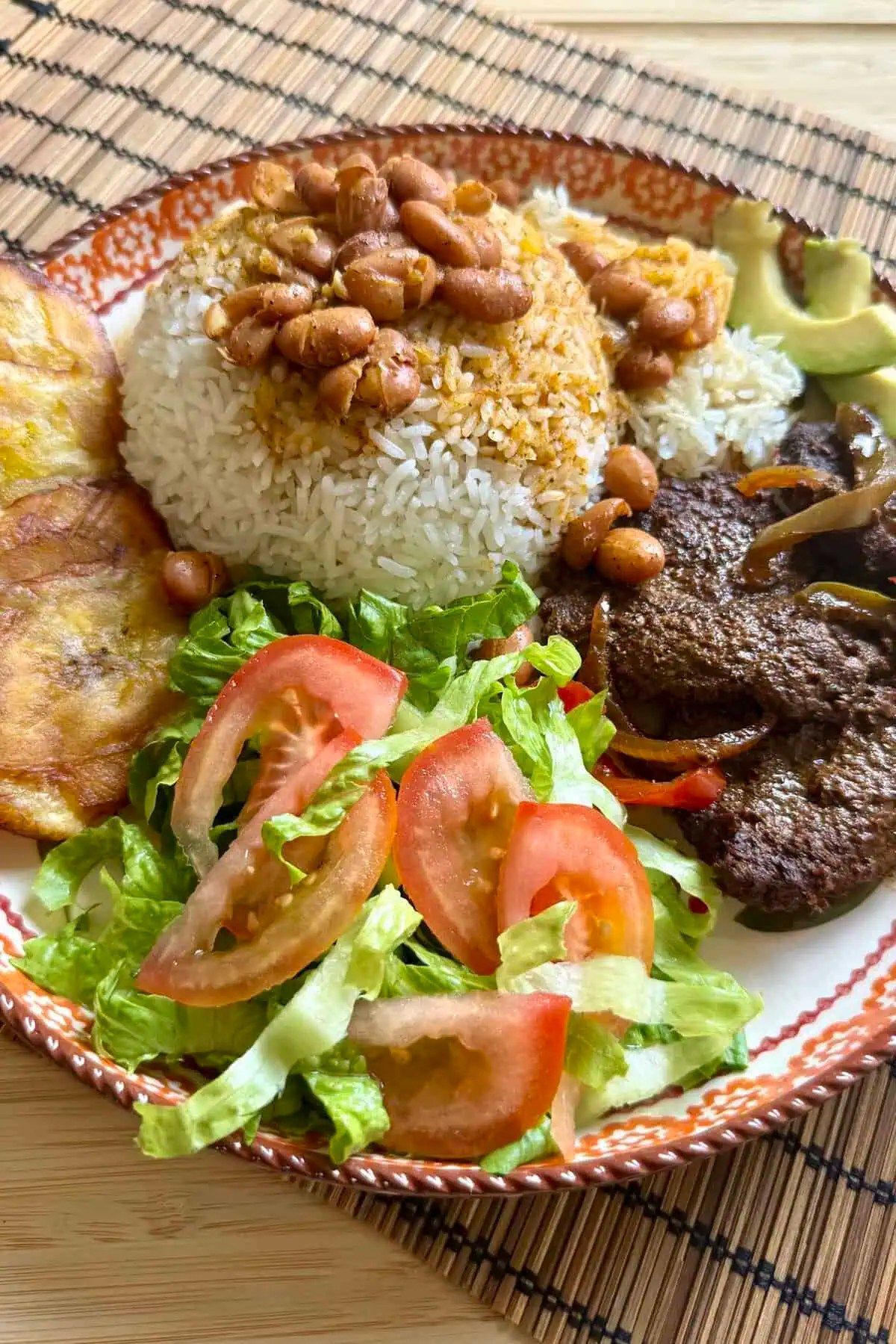 Plate with white rice, beans, steak, salad, fried plantains, and avocado.
