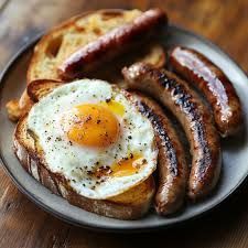 Plate of breakfast: fried egg on toast, sausages, and a piece of bread.
