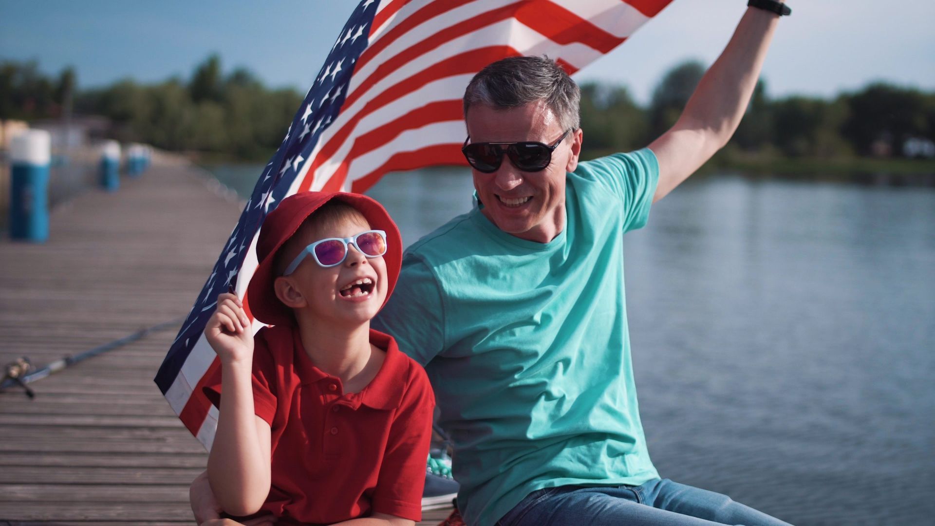 A man and a boy are sitting on a dock holding an american flag.