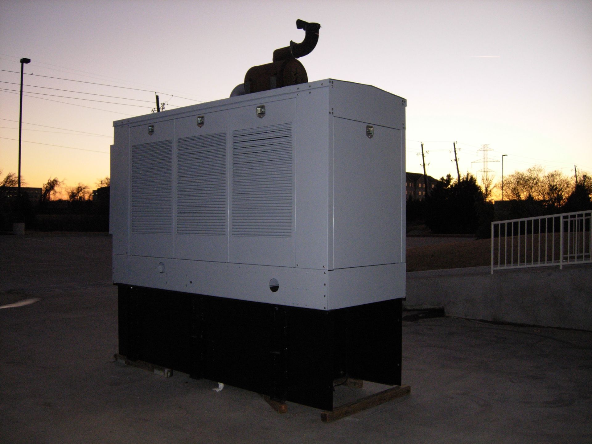 Generator in a white enclosure with black base outdoors at dusk.