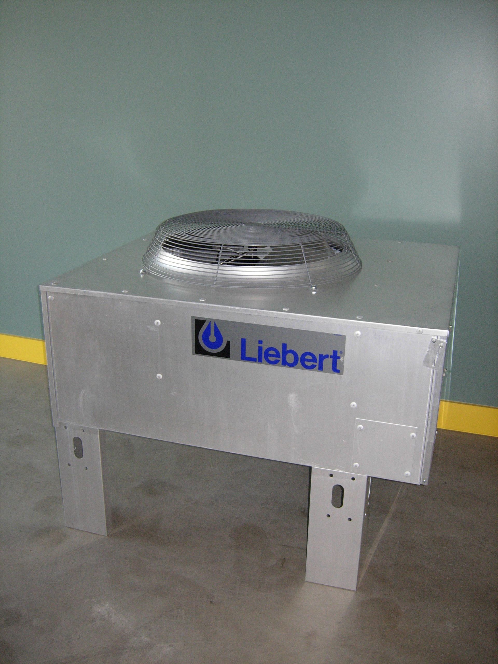 A Liebert cooling unit with a silver body, fan, and legs, against a grey and yellow wall.