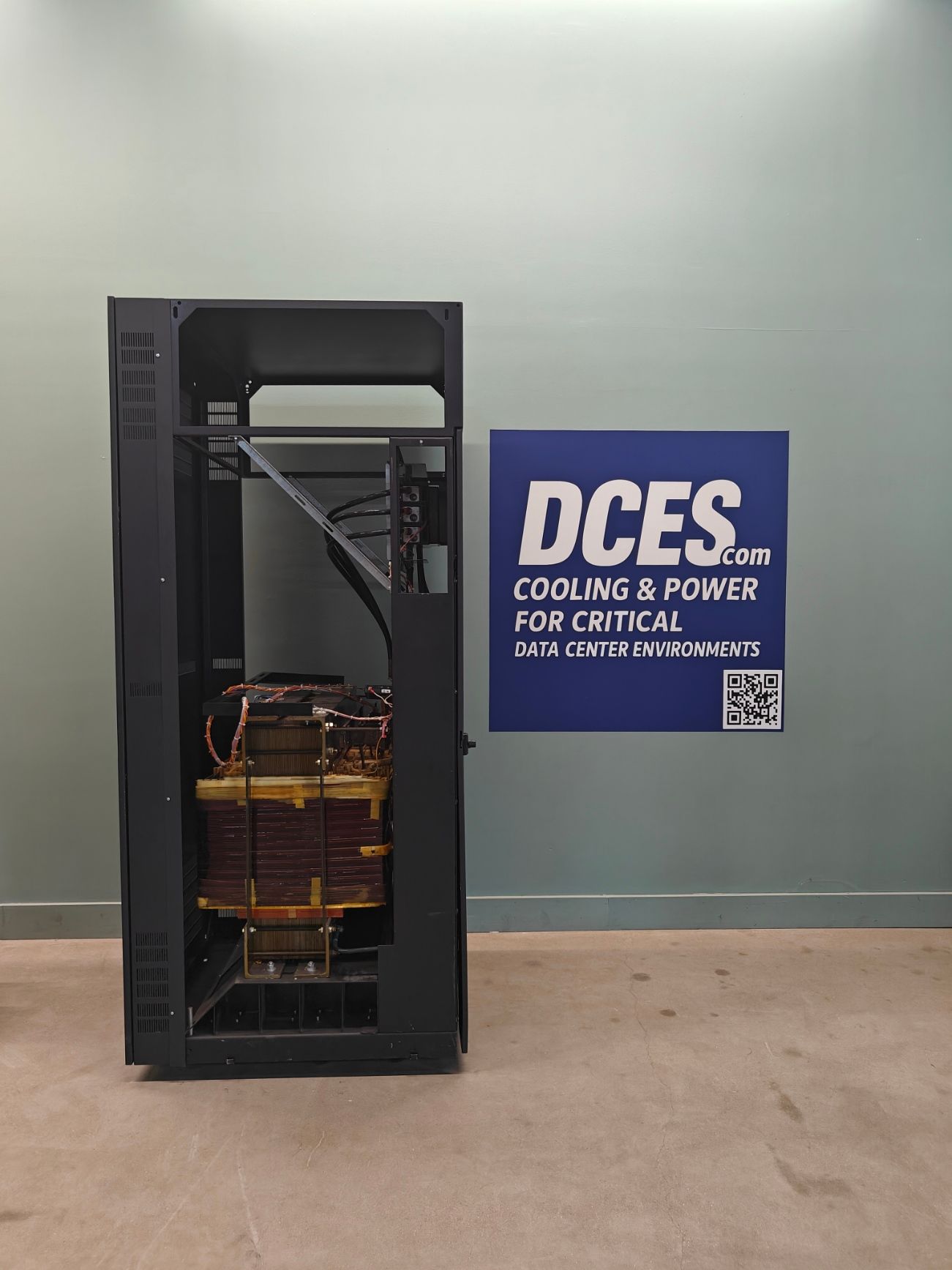 Black server rack, open, with large brown transformer inside, next to a sign for data center power.