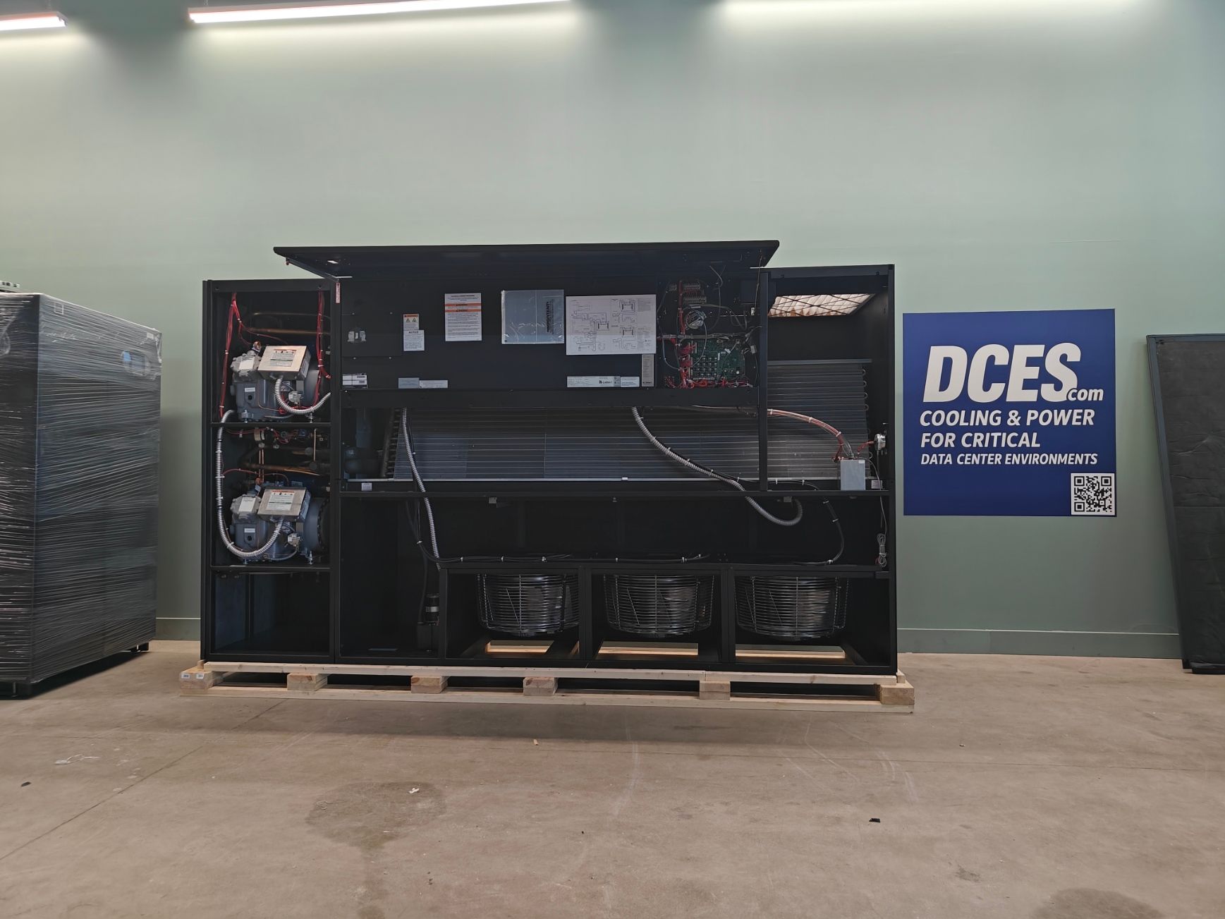 A large, open black electrical unit, likely HVAC, on a wooden pallet, indoors.