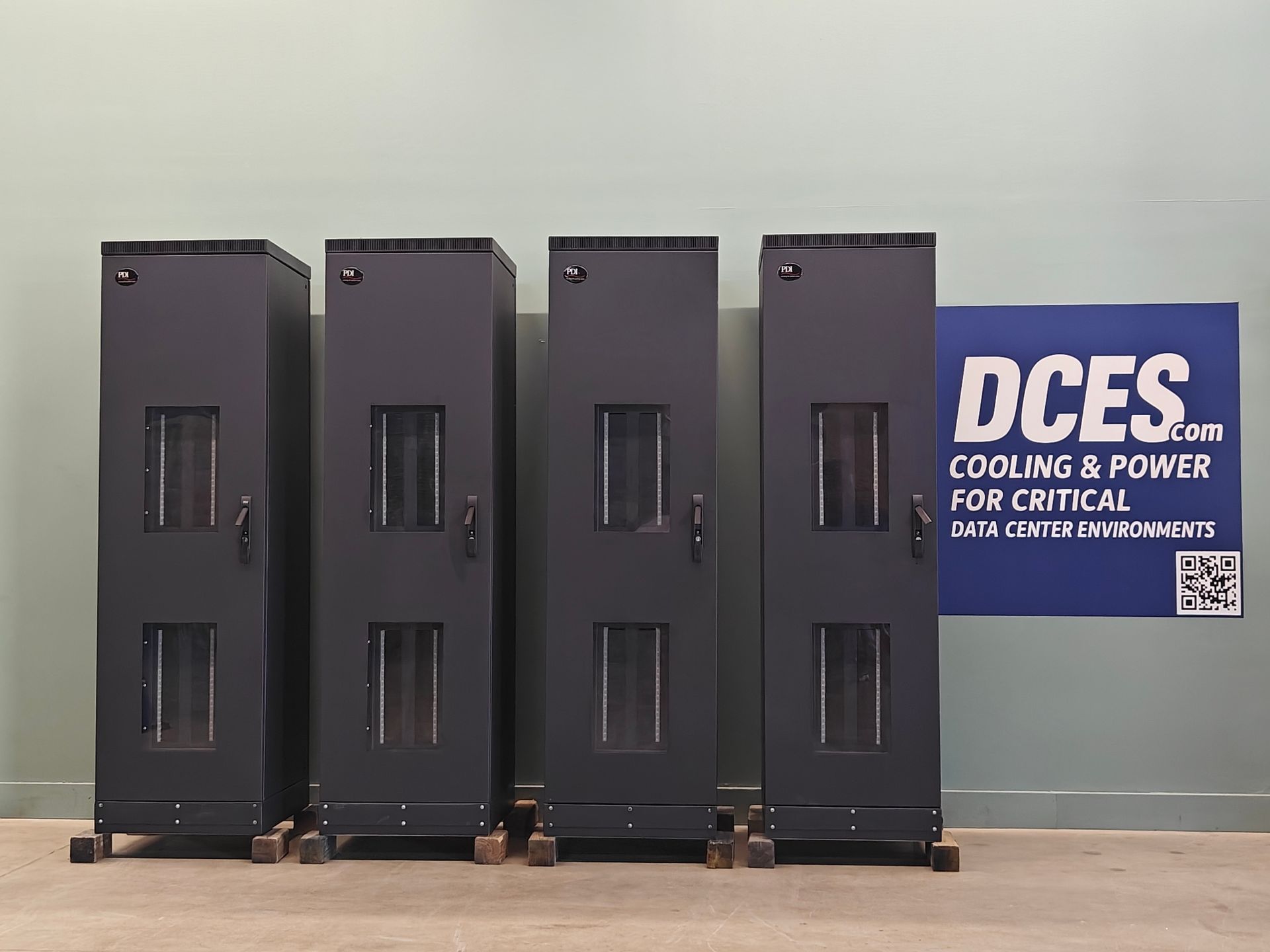 Four tall, black server racks on wheels, next to a sign for DCES.