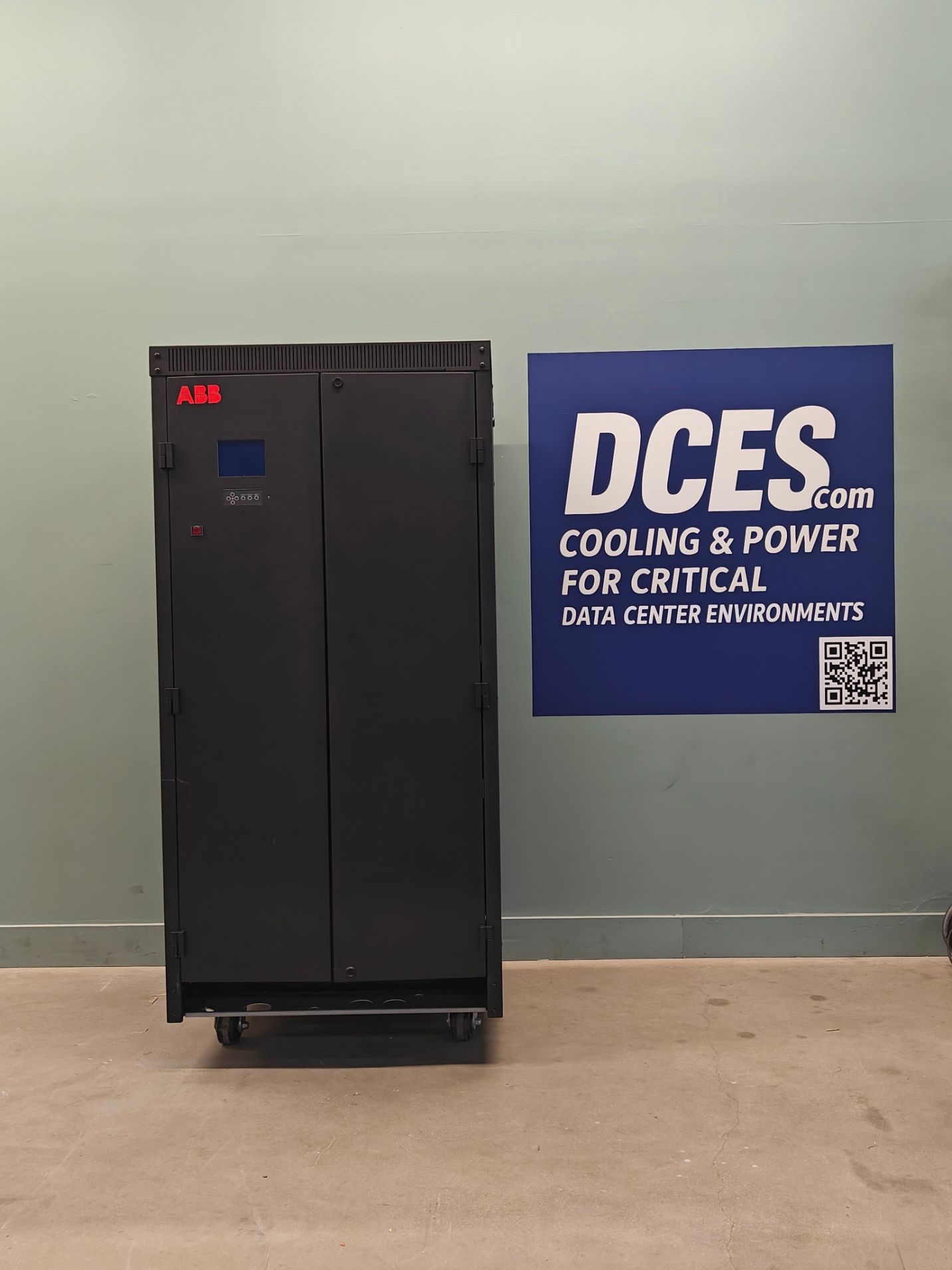 Dark gray UPS cabinet on wheels, next to a blue sign that says 