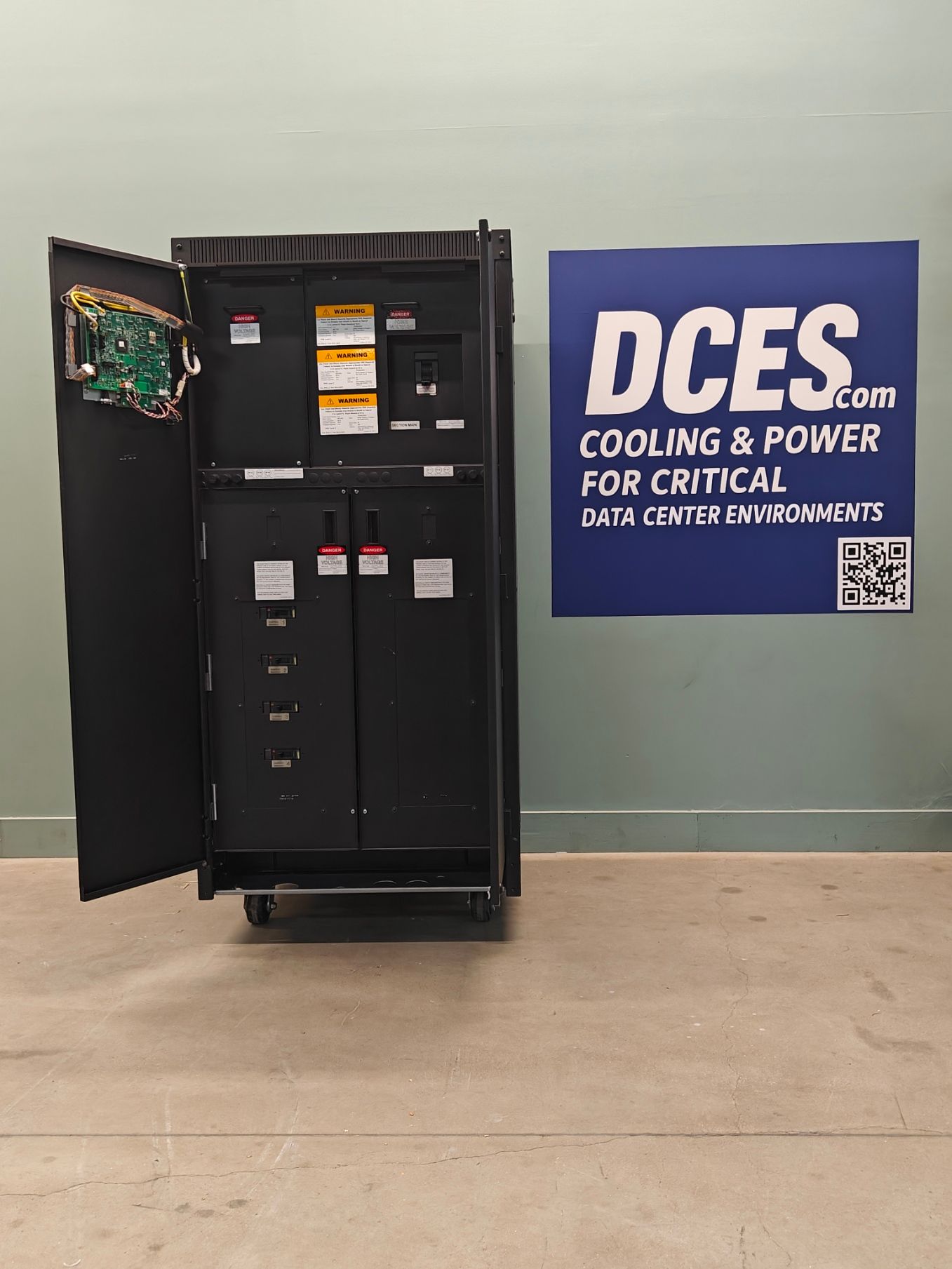 Black server cabinet on wheels with open door, inside a room, with a DCES.com sign.