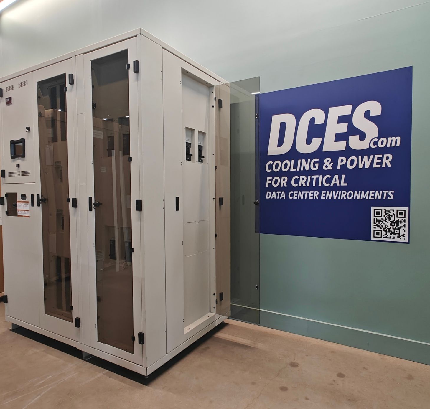 A large, white server cabinet with glass doors in front of a wall with a 