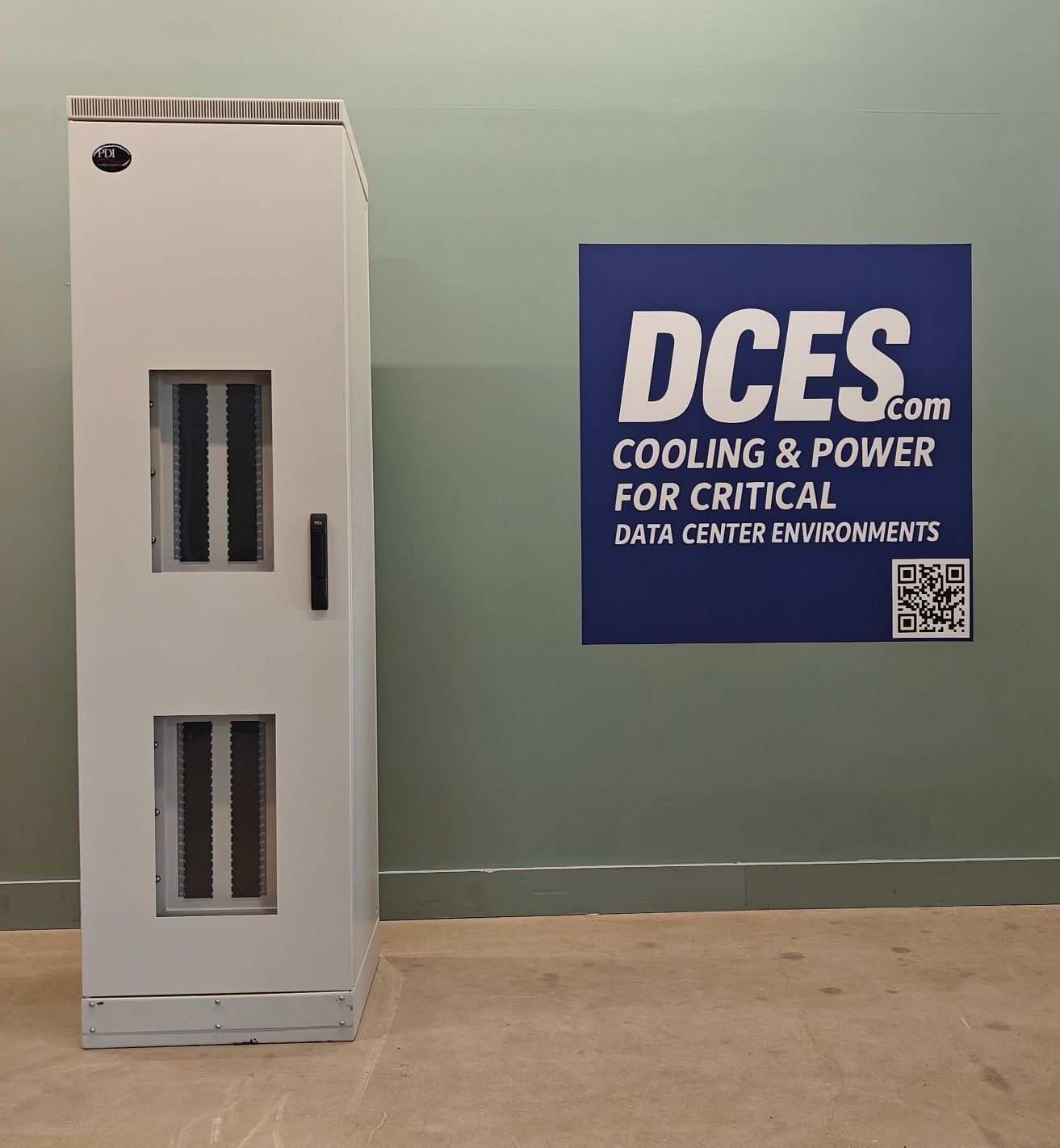 A tall, gray electrical cabinet with vents, next to a blue sign for DCES cooling & power.