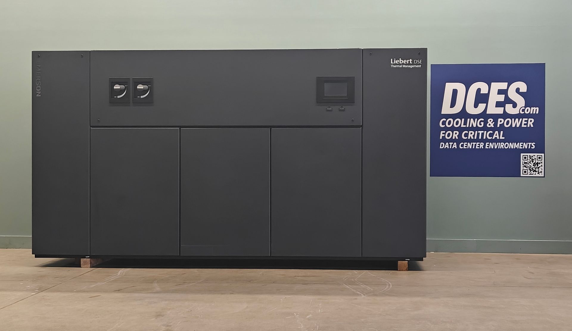 Dark gray equipment cabinet with control panels; blue sign says 