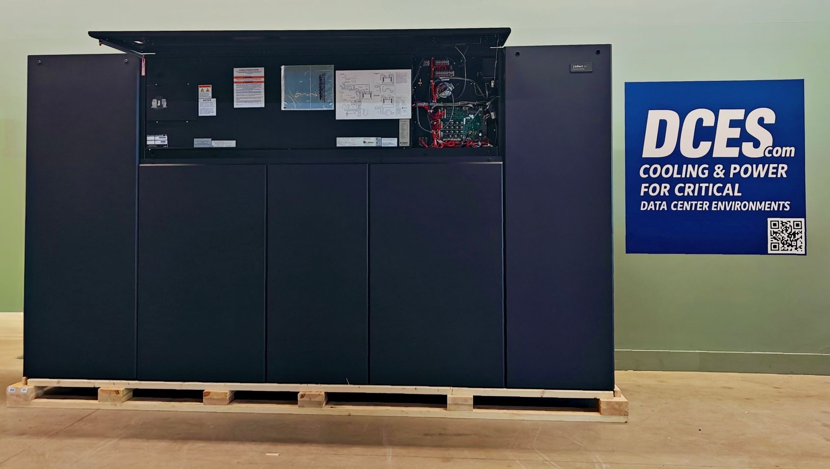 Black electrical equipment cabinet on a pallet, with open top panel, beside a DCES sign.